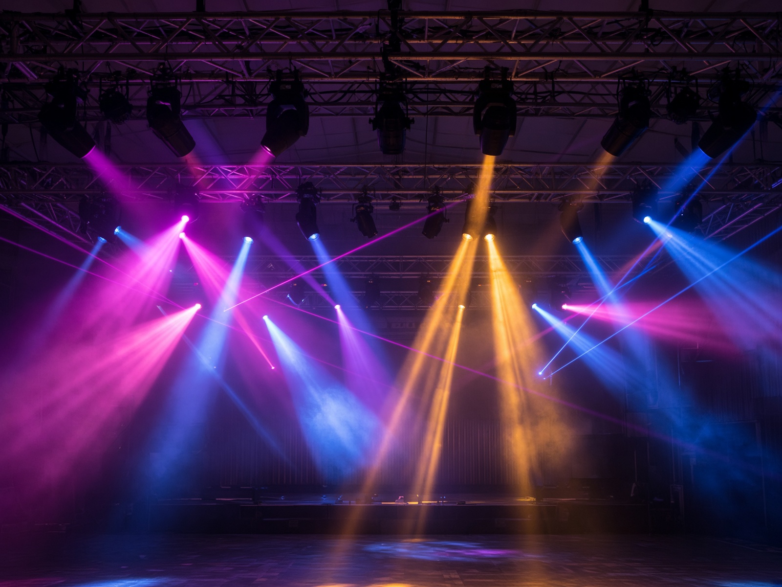 Overhead truss with colorful beams and lasers in haze.